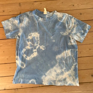 Blå tie-dye t-shirt - Säljer en blå och vit tie-dye t-shirt med klassisk passform. T-shirten har korta ärmar och rund halsringning. Perfekt för dig som gillar en avslappnad och trendig stil.