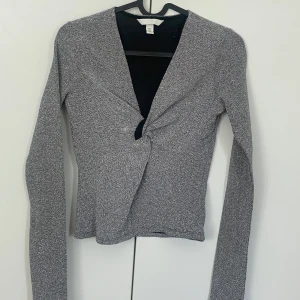 Grå omlottopp från H&M - Säljer en silver/glitter topp från H&M med lång ärm. Toppen har en v-ringad design och är tillverkad i ett mjukt, stretchigt material. Perfekt för fest. Ny utan prislapp