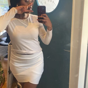 Vit omlottkjol i kort modell - Säljer en vit kortkjol med omlottdesign och bred linning. Kjolen har en stilren look och är figurnära med snygga skärningar framtill. Perfekt för dig som gillar minimalistisk stil.