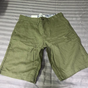 Olivgröna linneshorts från Dressmann - Snygga olivgröna shorts från Dressmann i linneblandning. Klassisk passform med knapp och dragkedja framtill, samt sidofickor och bakfickor med knapp. Perfekta för varma dagar och enkel att matcha med t-shirt eller skjorta.