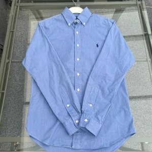 Ralph Lauren slim fit skjorta blå – Small - ( ÖPPEN FÖR BUD)                                                                                Säljer en superfräsch Ralph Lauren skjorta i slim fit modell, storlek Small. Färg: ljusblå, klassisk design med broderad Polo-logga och button-down krage. Nästan nyskick, endast använd få gånger. Perfekt till vardags, kontoret eller festen. 100% bomull – riktigt skön och sval!  Köpt för mycket mer, säljer till bra pris.
