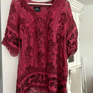 Rosa mönstrad klänning från Angie - Säljer en rosa klänning från Angie med svart blommigt mönster. Klänningen har v-ringning och korta ärmar, samt är tillverkad i ett lätt och luftigt material. Perfekt för varma dagar och har en bohemisk känsla.