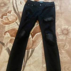 Svarta jeans med slitningar från Amiri - Säljer ett par svarta jeans från Amiri med slitna detaljer över knäna. Byxorna har klassisk femficksdesign, knappgylf och smal passform. Perfekta för dig . Size 32 