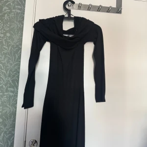 Svart off shoulder långklänning - Säljer en svart off shoulder långklänning i storlek S. Klänningen har lång ärm och en snygg draperad överdel som ger en elegant look. Slits vid ärmsluten. Perfekt för dig som vill ha en stilren och tidlös outfit. Den är ganska tjock i materialen/ stickad 