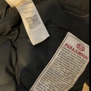 Dunjacka från Parajumper Right Hand S - Säljer en  dunjacka från Parajumpers med orange detaljer och patch på ärmen. Jackan har dragkedja och flera fickor,Perfekt för kyliga dagar och har en snygg, sportig look.