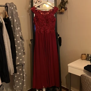 Röd balklänning - Elegant röd långklänning med vackra spetsdetaljer och broderier upptill. Perfekt för bal eller festliga tillfällen. Passar mig som är 165 med klackar på det. Köpt på Zalando 