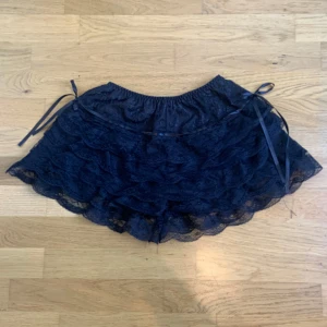 Svarta spets-shorts/bloomers med volanger och rosetter - Super söta nya och oanvända tunnare shorts/bloomers med flera lager volanger i spets och dekorativa rosetter i sidorna. Shortsen har elastisk midja :)💗