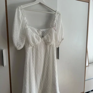Vit klänning med puffärmar - Superfin vit kortklänning från Missguided med puffiga kortärmar och diskret prickigt mönster i tyget. Perfekt för studenten. Aldrig använd och prislapp kvar!