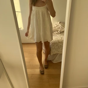 Vit kort klänning med blommor - Vit kortklänning med broderade blommor, väldigt tunn och perfekt för varma dagar! Klänningen har även små inbyggda shorts så den inte blåser upp!