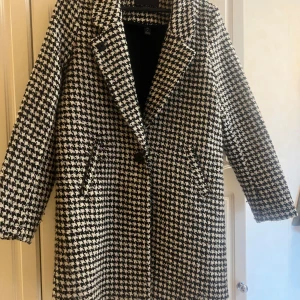 Svartvit rutig kappa från Scotch & Soda - Säljer en snygg svartvit kappa från Scotch & Soda i klassiskt rutigt mönster. Jackan har lång ärm, bred krage och två fickor framtill. Perfekt för dig som gillar tidlös stil med en twist.