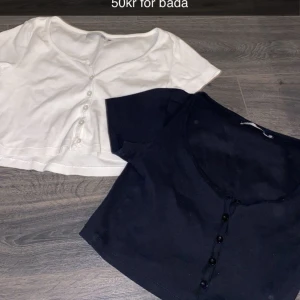 Två croppade toppar med knappar - Säljer två croppade toppar, en vit och en svart, båda med kort ärm och knappar framtill. Perfekta att matcha med jeans eller kjol för en enkel och stilren look. 30kr för båda 