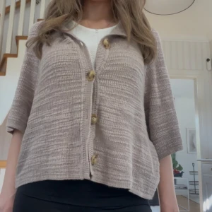 Beige stickad kofta med stora knappar - Säljer en beige stickad kofta med trekvartsärm och stora träknappar framtill. Koftan har en lös passform och är perfekt att slänga över en t-shirt. Supermjuk och enkel att styla till olika outfits.