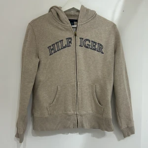 Beige hoodie från Tommy Hilfiger - Säljer en beige hoodie från Tommy Hilfiger!💕Mysig och passar till det mesta! Skulle dock säga att storleken lutar sig mer mot S än M. OBS! Dragkedjan är omvänd. Skriv till mig vid frågor!!