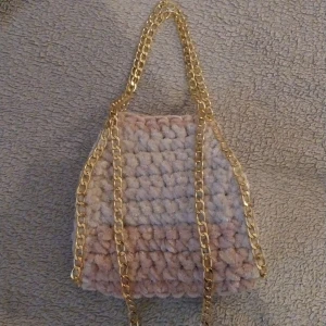 Rosabeige virkad väska med guldkedja - Unik rosabeige virkad handväska i mjuka pastellfärger med en elegant guldkedja. Perfekt för att ge din outfit en personlig touch. Väskan har en mysig och trendig design.
