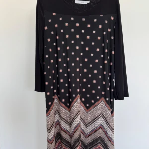 Svart mönstrad klänning - Snygg svart klänning med små vita och röda prickar samt ett zigzag-mönster i nederkant. Klänningen har långa ärmar och en bekväm passform. Perfekt för en stilfull look.