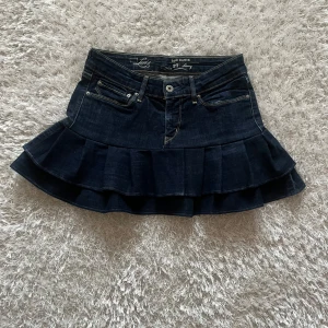 Mörkblå jeanskjol med volang - En lågmidjad jeanskjol omsydd från ett par jeans Midjemått tvärsöver - 36 cm Längd - 33 cm