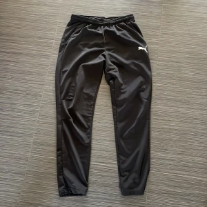 Svarta träningsbyxor från Puma - Säljer ett par svarta träningsbyxor från Puma. Byxorna har en elastisk midja och en smal passform som ger en sportig look. Perfekta för träning eller en avslappnad dag.