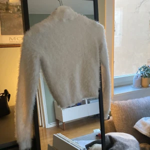 Vit fluffig tröja - Säljer en supermjuk och fluffig vit tröja med lång ärm. Perfekt för att hålla sig varm och stilren under kyliga dagar. Tröjan har en croppad design som ger en modern touch. Passar perfekt till både jeans och kjol.