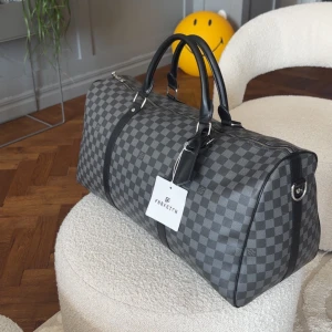 Louis Vuitton dufflebag (keepall) - ⚠️ Intressekoll ⚠️ Snygg rutig dufflebag från Louis Vuitton i grått och svart. Väskan har ett klassiskt mönster och är utrustad med dragkedja och svarta handtag. Perfekt för resan eller som en stilren accessoar till vardags.