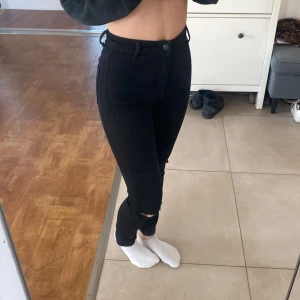 Svarta skinny jeans - Säljer ett par svarta skinny jeans med hög midja. De har en snygg slitning vid knäna och stängs med dragkedja och knapp. Perfekta för en stilren look. Storleken motsvarar xs