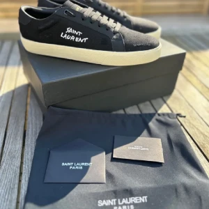Svarta sneakers från Saint Laurent - Snygga svarta sneakers från Saint Laurent med vit sula och märkets logga på sidan. Skorna har snörning och en klassisk rund tå. Perfekta för en stilren look.