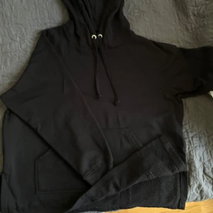 Svart hoodie med slits på sidorna  - Säljer en svart hoodie med slits på sidorna och justerbar huva från H&M. Passar bra till jeans eller mjukisbyxor. Fick den som present och har knappt använt den.