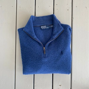 Blå tröja från Polo Ralph Lauren - Säljer en snygg blå tröja från Polo Ralph Lauren med dragkedja vid halsen. Tröjan är långärmad och har en klassisk design med ribbade muddar vid ärmslut och nederkant. Perfekt för kyligare dagar!