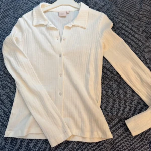 Vit ribbad kofta från nelly - Säljer en stilren vit ribbad kofta från nelly. Den har långa ärmar och knappar framtill, perfekt för lager-på-lager-stil. Passar både till vardags och mer uppklädda tillfällen. Ett måste i garderoben! 🤍 Aldrig använd!