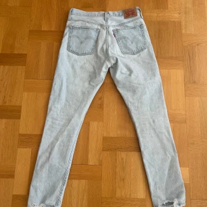 Ljusblå jeans från Levi's - Snygga ljusblå 501 jeans från Levi's med klassisk femficksdesign och knappgylf. Perfekta för en avslappnad stil. Märkeslappen i brunt läder sitter baktill i midjan.