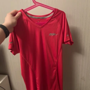 Röd träningst-shirt från Nike - Säljer en röd träningst-shirt från Nike med v-ringning och korta ärmar. Perfekt för löpning eller gymmet. T-shirten har en reflekterande logga på bröstet och är tillverkad i ett lätt och andningsbart material.