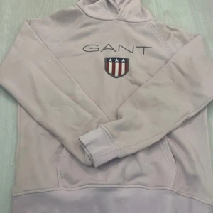 hoodie från GANT - Säljer en snygg hoodie från GANT med broderad logga och emblem på bröstet. Har tyvärr en liten fläck på fickan som man kan se på en bild, men inget man tänker på. Hör av er för fler bilder och frågor🥰