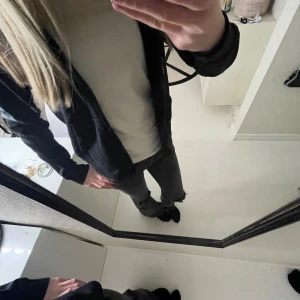 Svart jacka med dragkedja från stronger - Säljer en svart stronger kofta med dragkedja och långa ärmar. Jackan har ett diskret mönster på ärmarna och en normal passform. Perfekt för vardagsbruk.