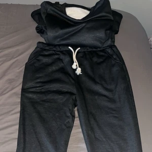 Svart mjukissett med snörning - Säljer ett par svarta mjukisbyxor och tröja med vit snörning i midjan. Settet har en avslappnad passform och är perfekta för en bekväm dag hemma. Insidan är fodrad med mjukt material för extra komfort. Helt oanvända då jag fick de i en mystery box. 150kr per plagg