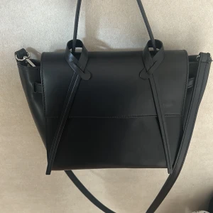 Svart väska - Snygg svart väska med kort och långt band. Praktisk och rymlig med innerfack. Säljer den för att den inte kommer till användning på grund av att jag har andra väskor. Använd ett fåtal gånger.  