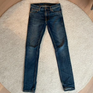 Blå lean Dean från Nudie Jeans - Snygga blå jeans från Nudie Jeans med en klassisk femficksdesign och knappgylf. De har en slim passform och är tillverkade i denim med en lätt tvättad look. Perfekta för en stilren vardagslook.