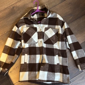 Brun och vit rutig jacka från H&M Divided - Säljer en snygg brun och vit rutig jacka från H&M Divided. Jackan har långa ärmar och knappar framtill. Två stora bröstfickor. Perfekt för höst och vår!