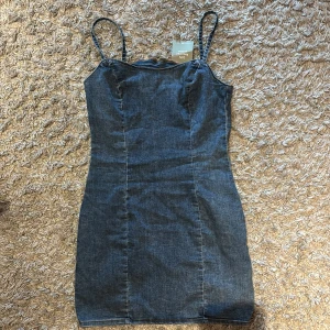 Blå jeansklänning från H&M Divided - Snygg blå jeansklänning från H&M Divided med smala axelband och dragkedja bak. Lappen är kvar då den aldrig blivit använd
