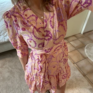 Mönstrad klänning med volangdetaljer - Denna superfina klänningen är från Sandro med ett fint blommigt tryck! Den är tunn och i ett blankt material. Färgerna passar superbra till sommaren när man är brun!🧡💖