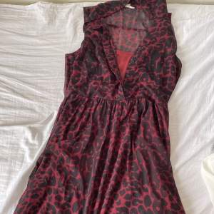 Snygg leopardmönstrad klänning i rött och svart med knappar framtill. Klänningen har en ärmlös design och ett lätt transparent tyg som ger en cool look. Perfekt för en kväll ute eller en speciell tillställning.