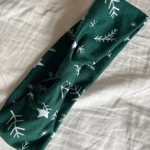 Grönt diadem från The Body Shop - Snyggt grönt diadem med vita snöflingor och stjärnor, perfekt för vintersäsongen. Tillverkat av 95% polyester och 5% elastan för en bekväm passform. Aldrig använd 