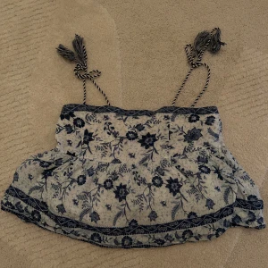 Blommig linnetopp från Pepe Jeans - Söt blommig linnetopp från Pepe Jeans i blått och vitt. Toppen har tunna axelband med tofsdetaljer och ett vackert blommönster!