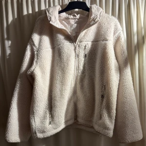 Vit teddyjacka från H&M - Mysig vit teddyjacka från H&M med dragkedja och huva. Perfekt för kyliga dagar med sin fluffiga och varma design. Jackan har en normal passform och är långärmad, vilket gör den idealisk för höst och vinter. Mycket sparsamt använd
