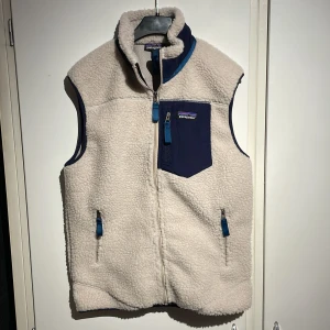 Beige fleeceväst från Patagonia - Säljer en mysig beige fleeceväst från Patagonia med blå detaljer. Västen har dragkedja fram och praktiska fickor med blå dragkedjor. Perfekt för lager-på-lager under kyliga dagar. Passar väldigt bra nu till våren! Västen är använd endast 1 gång.