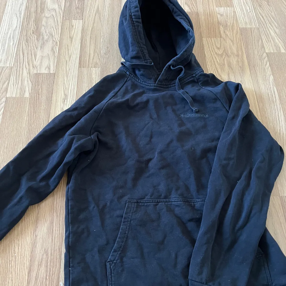 Säljer en svart hoodie från Peak Performance. Den har en klassisk design med en stor ficka framtill och justerbar huva. Perfekt för en avslappnad stil. Ett lite hål i luvan. Neuletakit & Villapaidat.