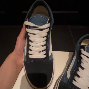Blå och svarta sneakers från Vans - Snygga sneakers från Vans i en cool kombination av blått och svart. Skorna har den klassiska vita sidoremsan och vita snören. Perfekta för en avslappnad stil.