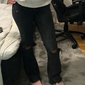 Svarta flare jeans från Bershka - Snygga svarta flare jeans från Bershka med slitna detaljer vid knäna. Perfekta för en trendig look. De har en klassisk femficksdesign och är tillverkade i denim.