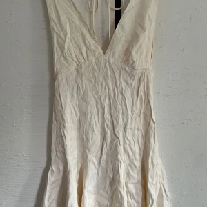 Vit omlottklänning med v-ringning - Säljer en vit klänning från H&M i storlek XS. Klänningen har djup v-ringning både fram och bak samt knytband i nacken. Perfekt för sommarens varma dagar.