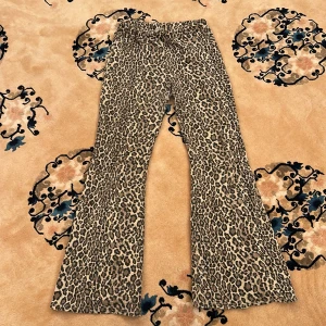 Leopardmönstrade bootcut byxor - Säljer ett par snygga leopardmönstrade byxor med bootcut passform. Byxorna har hög midja och är perfekta för dig som vill sticka ut med ett djurmönster. Supercoola att styla med en enkel topp eller hoodie.