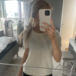 Vit stickad kortärmad tröja - Säljer en enkel och stilren vit stickad tröja med korta ärmar. Tröjan har en rund halsringning och är mjuk i materialet, perfekt för lager-på-lager eller sommarens svalare dagar.