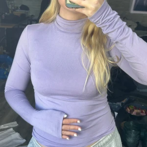 Ljuslila polotröja - Säljer en ljuslila polotröja med lång ärm och tight passform. Tröjan är enkel och stilren, perfekt att matcha med olika outfits. Materialet känns mjukt och stretchigt. 